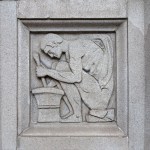 Stone wall relief depicting a seated figure using a mortar and pestle, representing pharmacy or chemistry.
