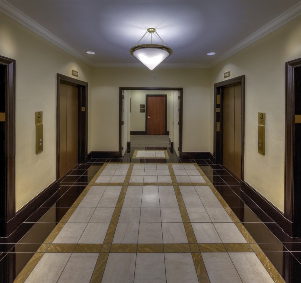 Modern elevator lobby with polished tiled flooring, dark wood accents, and a triangular ceiling light.