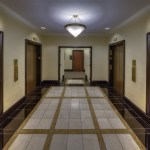 Modern elevator lobby with polished tiled flooring, dark wood accents, and a triangular ceiling light.