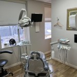 Modern dental treatment room with a patient chair, medical equipment, and a window.