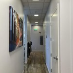 Bright, narrow hallway in a professional office with wood flooring and wall art.