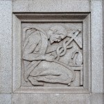 Stone wall relief depicting a kneeling figure holding a caduceus, the traditional symbol of medicine.